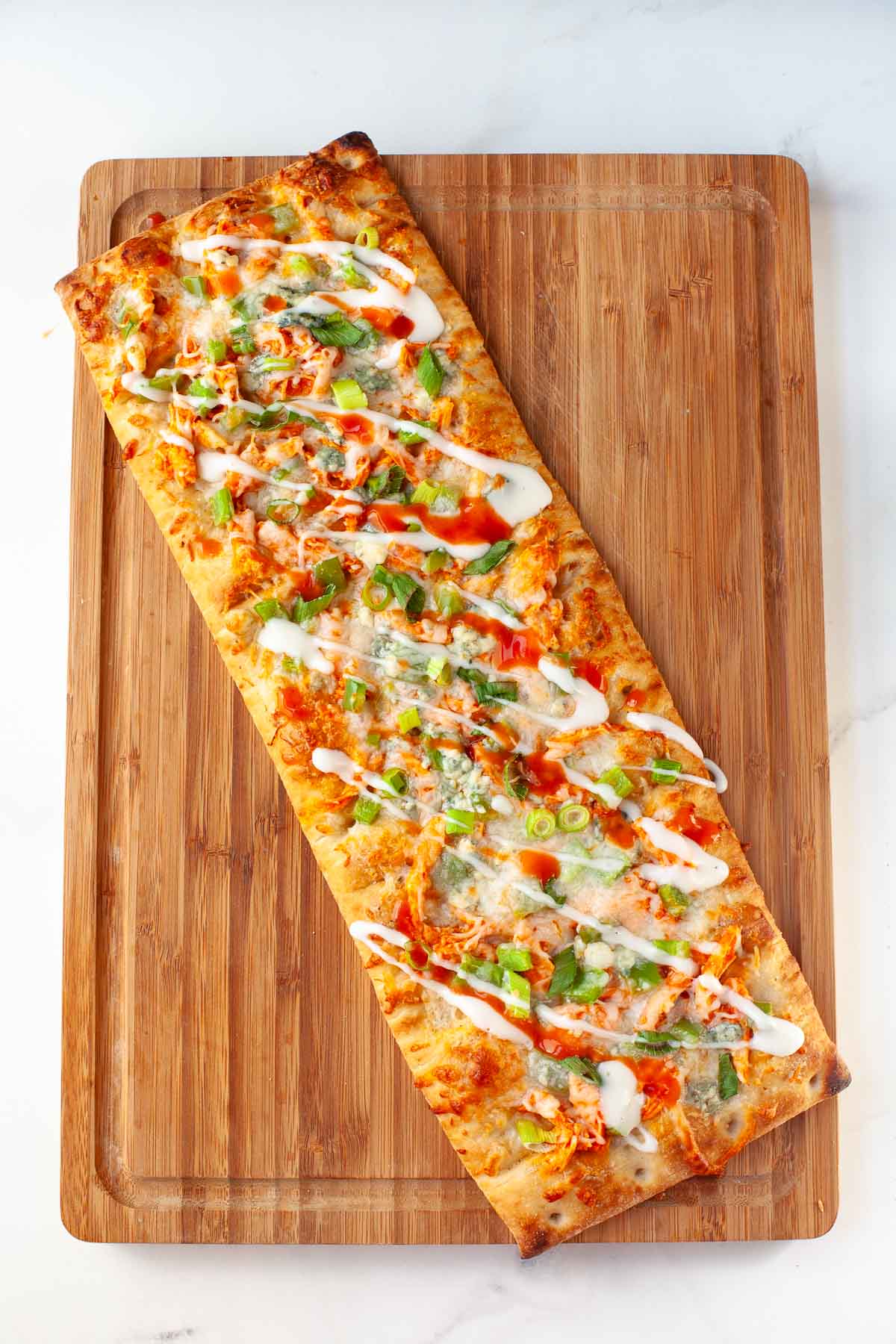 baked buffalo chicken flatbread with ranch dressing and hot sauce drizzled on top on wood cutting board